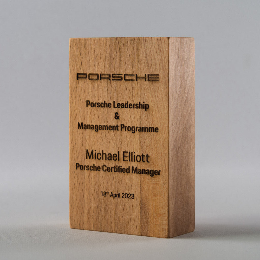 Wooden plaque with Porsche branding and engraved text on a gray background